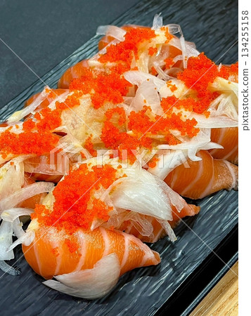 Fresh salmon sushi with bright orange slices placed on top of perfectly shaped rice, garnished with green leaves and radish for a simple, colorful, and appetizing presentation 134255158