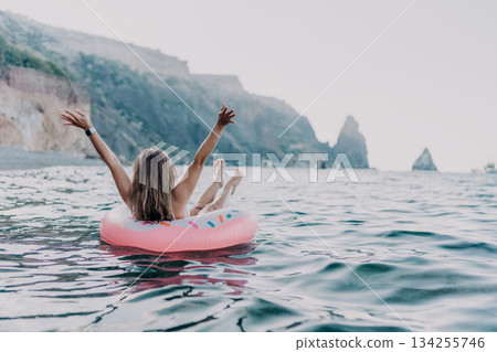 Woman, floating, sea. Relaxed woman enjoying summer vacation on a donut inflatable ring near rocky cliffs. Woman, floating, sea. Relaxed woman enjoying summer vacation on a donut inflatable ring near rocky cliffs. 134255746