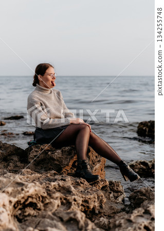 Woman Sea Coast Autumn: Contemplative Pose, Rocky Seashore, Seasonal Solitude. Woman Sea Coast Autumn: Contemplative Pose, Rocky Seashore, Seasonal Solitude. 134255748