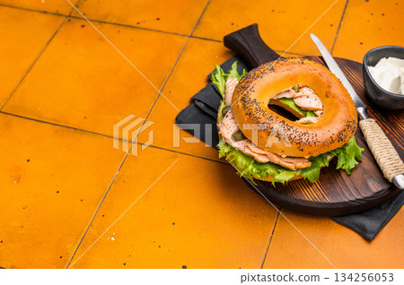 Breakfast Bagel with smoked salmon, lettuce and cream cheese on a wooden board. orange background. top view 134256053