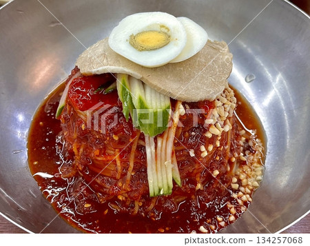 Naengmyeon, a refreshing Korean cold noodle dish served in an icy broth, topped with sliced vegetables, a boiled egg, and spicy sauce. Perfect for summer food photography and Korean cuisine projects. 134257068