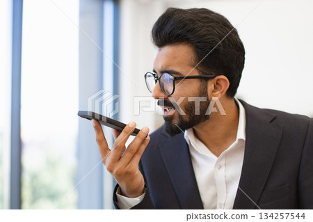 An Indian businessman wearing glasses is talking on his smartphone in an office setting 134257544