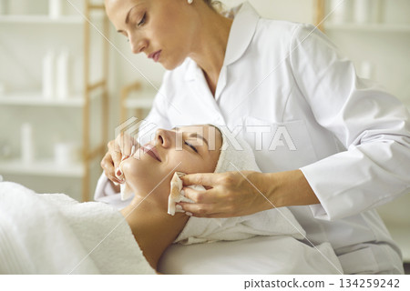 Cosmetologist at beauty parlor uses wet wipes to remove makeup from woman's face 134259242