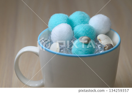 Summer decoration of seashells and blue pom-poms in a mug Summer decoration of seashells and blue pom-poms in a mug 134259357