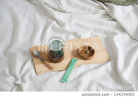 Healthy green drink and supplement capsule on small wooden tray on white blanket. Healthy green drink and supplement capsule on small wooden tray on white blanket. 134259363