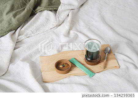 Cozy morning scene with bed, green chlorophyll drink, health vitamin pills. 134259365