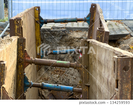 Robust metal trench shoring system with rusty panels and adjustable struts secures a deep excavation ditch, vital for construction safety and infrastructure projects Robust metal trench shoring system with rusty panels and adjustable struts secures a deep excavation ditch, vital for construction safety and infrastructure projects 134259593