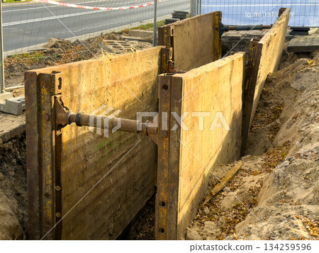 Robust metal trench shoring panels installed in an open excavation, providing critical worker safety for urban infrastructure construction, eye-level perspective 134259596