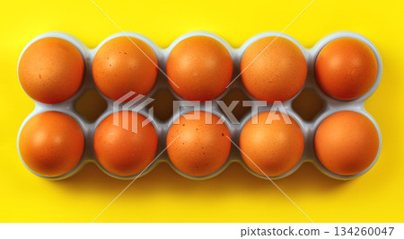 Ten beige eggs in plastic holder from fridge on yellow board, view from above Ten beige eggs in plastic holder from fridge on yellow board, view from above 134260047