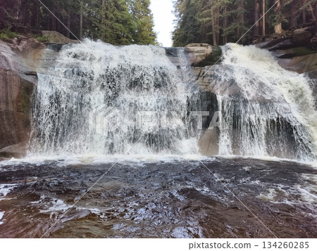 immense waterfall pouring into calm shallow water surrounded by verdant trees and rocky formations immense waterfall pouring into calm shallow water surrounded by verdant trees and rocky formations 134260285