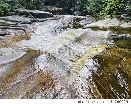 steady water glides over rock, natural water slide with reflective surface and flowing ribbons 134260329