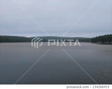 calm overcast water vista, peaceful water surface with distant woodland silhouette and subtle ripples calm overcast water vista, peaceful water surface with distant woodland silhouette and subtle ripples 134260453