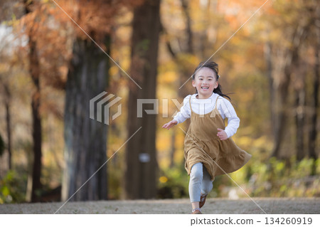 一張充滿活力的正面照，展現了一個女孩在落葉滿地的公園裡奔跑的快樂身影，捕捉到了她燦爛的笑容和純真無邪的氣質。 134260919