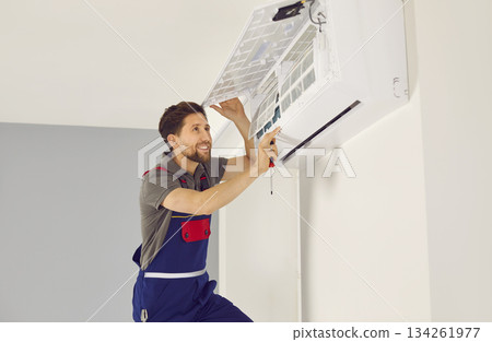 Portrait of smiling electrician with screwdriver maintaining air conditioner indoors. Portrait of smiling electrician with screwdriver maintaining air conditioner indoors. 134261977
