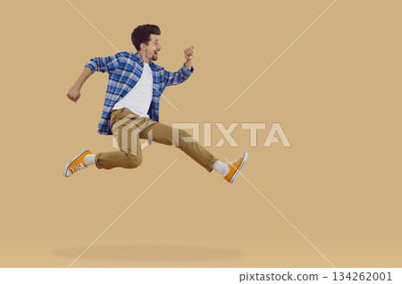 Happy brunette young man in casual clothes jumping in air on beige background, side view. Happy brunette young man in casual clothes jumping in air on beige background, side view. 134262001