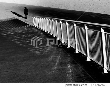 Silhouette of a lone man walking beside a curved railing in grayscale urban street scene Silhouette of a lone man walking beside a curved railing in grayscale urban street scene 134262820
