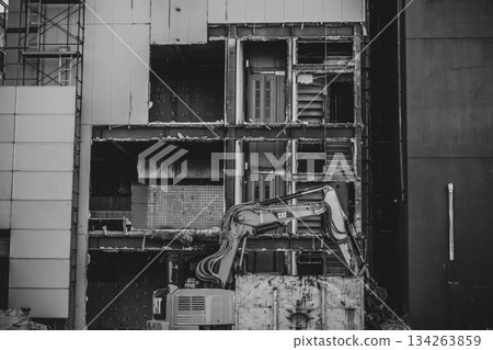 Monochrome: Heavy machinery demolishing the wall of a building Monochrome: Heavy machinery demolishing the wall of a building 134263859