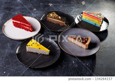 Assorted Cake Slices On Dark Slate Plates Create Colorful Dessert Display For Party 134264157