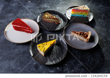 Assorted Cake Slices On Dark Slate Plates Create Colorful Dessert Display For Party 134264159