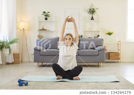Yogi old sporty senior woman practicing arm stretching, yoga at home, sitting exercise, relax pose 134264179
