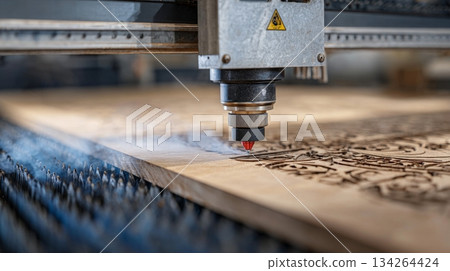 Precision laser cutting machine engraving intricate patterns into wood surface, showcasing craftsmanship and technology 134264424