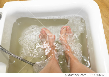 Foot bath concept, elderly woman doing a hygienic foot soak in water for soft foot skin in a beauty salon, spa pedicure 134266329