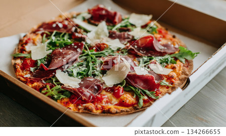 Gourmet pizza topped with fresh greens, cured meats, and shaved cheese in an open branded box, perfect for National Pizza Day celebration 134266655