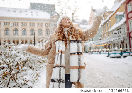 Young happy woman in a winter coat and scarf walks along a snowy city street. Concept of style. 134266788