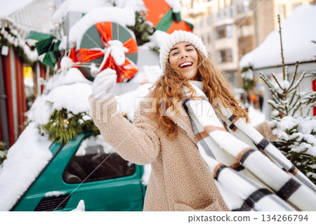 Smiling woman in a scarf and hat is having fun at a street holiday fair. Christmas concept. 134266794
