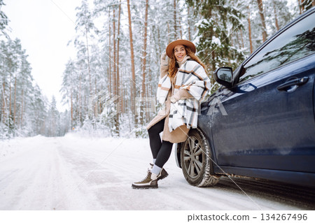 Beautiful young woman near a car in a snowy forest. First snow, great mood. Concept of vacation. Beautiful young woman near a car in a snowy forest. First snow, great mood. Concept of vacation. 134267496