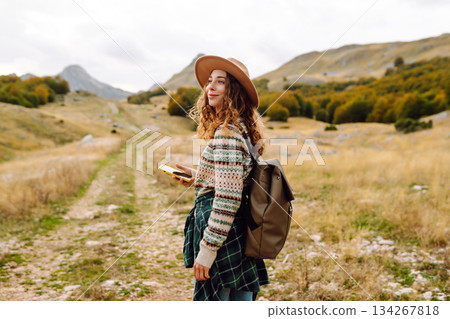 Woman is seen smiling, holding yellow phone in autumn landscape. Enjoying fresh air after hiking. 134267818