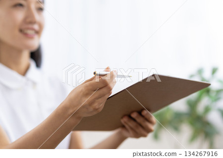 Close-up of a binder and pen held by a woman in a white coat Close-up of a binder and pen held by a woman in a white coat 134267916