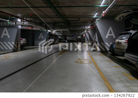 Underground Parking Garage A Level With Parked Cars, Wide Aisles, And Industrial Lighting Underground Parking Garage A Level With Parked Cars, Wide Aisles, And Industrial Lighting 134267922