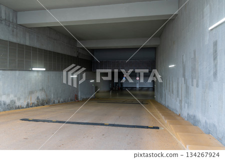 Underground Parking Ramp With Dim Concrete Walls, Long Corridor, And Bright Lighting 134267924