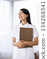 A woman in a white coat smiling and holding a binder by the window 134268341