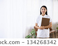 A woman in a white coat smiling and holding a binder by the window 134268342
