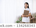 A woman in a white coat smiling and holding a binder by the window 134268343