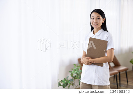A woman in a white coat smiling and holding a binder by the window 134268343