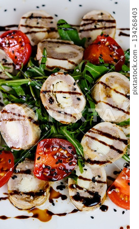 Step by step salad preparation with sliced chicken and liver rolls on a bed of arugula topped with tomato slices black and white sesame and a drizzle of olive oil in a bright kitchen 134268403