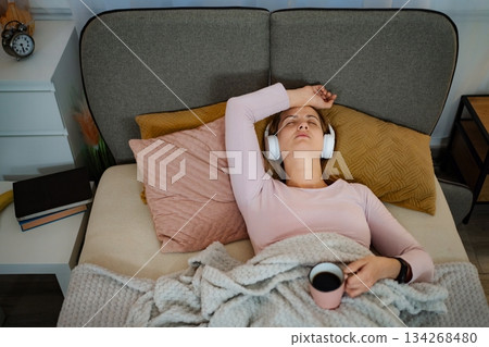 Woman relaxing in bed listening to music 134268480