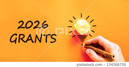 2026 Grants symbol. Concept words 2026 Grants on beautiful orange paper. Beautiful orange paper background. Light bulb icon. Businessman's hand with pen. Business and 2026 grants concept. Copy space. 134268730