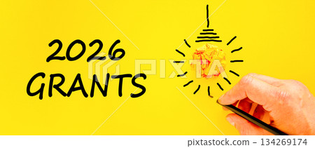 2026 Grants symbol. Concept words 2026 Grants on beautiful yellow paper. Beautiful orange paper background. Light bulb icon. Businessman's hand with pen. Business and 2026 grants concept. Copy space. 134269174