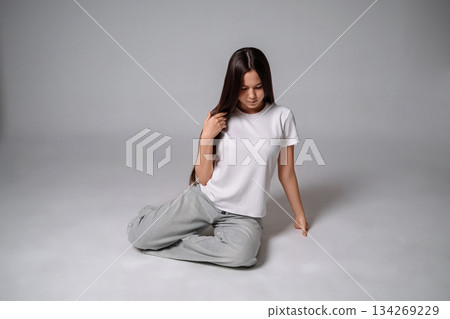 Teenager white t-shirt sitting contemplating quietly on gray studio floor with copy space 134269229