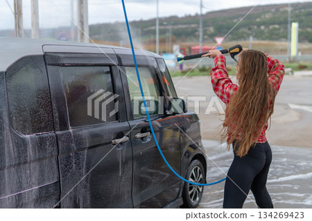 Car wash woman using high pressure spray gun cleaning dirty vehicle outdoors Car wash woman using high pressure spray gun cleaning dirty vehicle outdoors 134269423