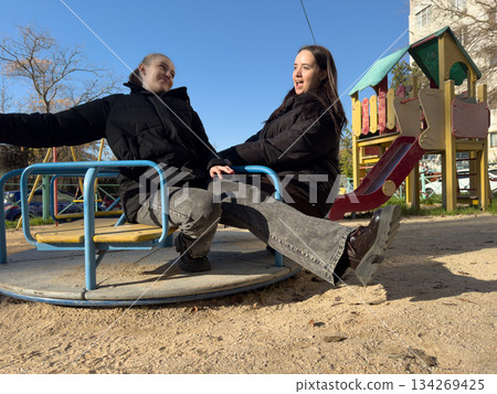 Women friends playground spinning two laughing young women enjoying spinning ride in urban park on sunny day Women friends playground spinning two laughing young women enjoying spinning ride in urban park on sunny day 134269425