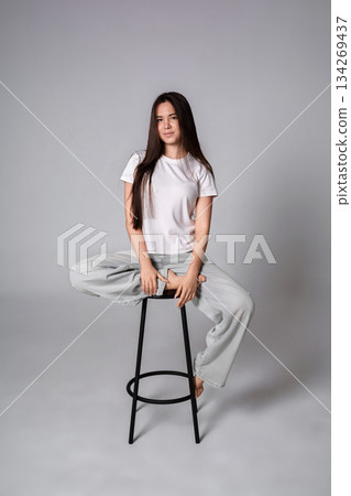 Young woman studio stool pose, fashionable casual girl sitting cross legged with copy space 134269437