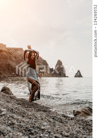 Woman Beach Pose Rocks - A woman poses on a rocky beach with the ocean in the background. Woman Beach Pose Rocks - A woman poses on a rocky beach with the ocean in the background. 134269552