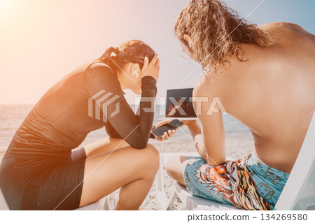 Couple Beach Laptop - Working remotely on the beach with a laptop during their vacation. Couple Beach Laptop - Working remotely on the beach with a laptop during their vacation. 134269580