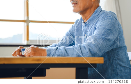 Senior man holding a teacup by the window 134270218