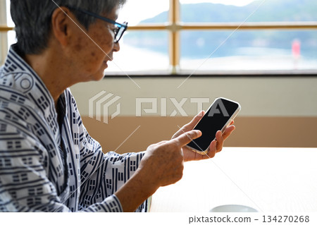 An elderly person in a yukata is operating a smartphone 134270268